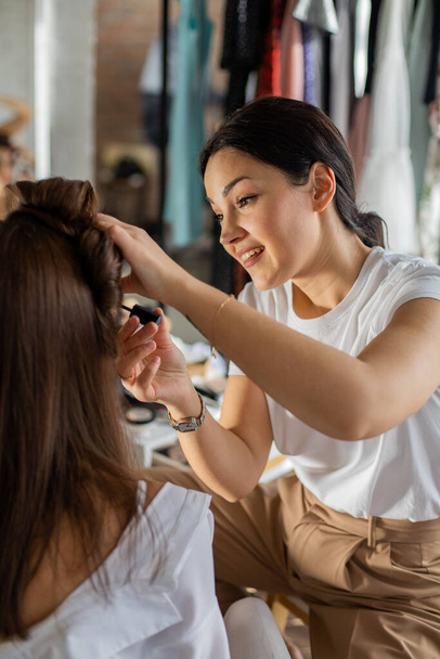 Woman visagist applying makeup cosmetic to female client getting ready at home. Make up artist working dye procedure. Two lady friends spending time together preparation at wardrobe roo - Photo, Image
