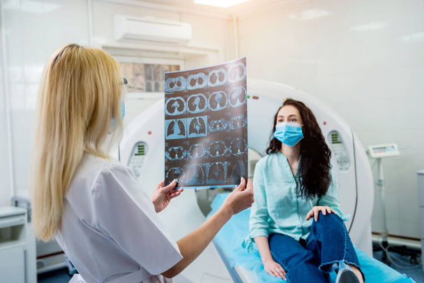 Radiologist with a female patient wearing protective masks examining a CT scan - Photo, image