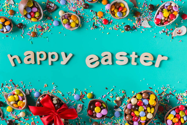 Easter frame with chocolate eggs and sweets on a pink background. Happy easter text. Top view, flat lay - Photo, Image