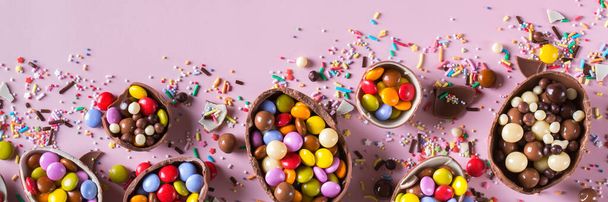 ピンクの背景にチョコレートの卵とお菓子とイースターフレーム。バナー、トップビュー、フラットレイアウト - 写真・画像