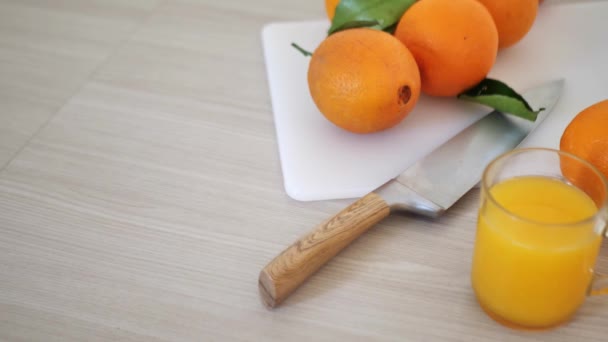 Vers sinaasappelsap in een glas omringd door sinaasappels op een grijze achtergrond - Video