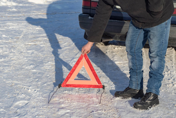 φωτισμός δρόμου. Λευκό χιόνι. Ο άνθρωπος βάζει μια πινακίδα έκτακτης ανάγκης. Βλάβη στο όχημα. - Φωτογραφία, εικόνα