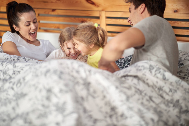 Kids having fun in the bed with their parents on a beautiful morning. Family, home, together - Фото, изображение