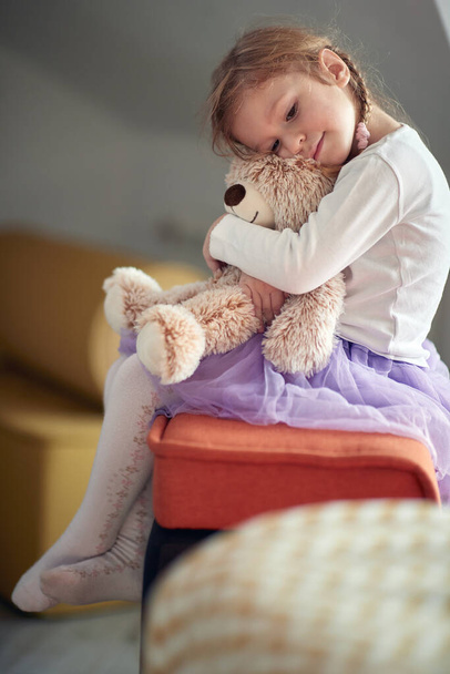 A little girl sitting on the bed in a hug with her teddy bear in a carefree atmosphere of home. Child, home, playing - Foto, Bild