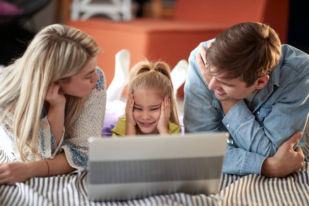 Mom and Dad watching laptop content with their little daughter in a relaxed atmosphere at home. Family, home, togetherness - 写真・画像