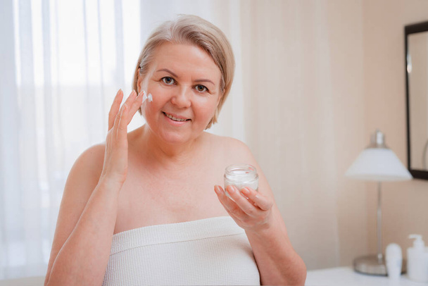 Seniorin Anti-Aging-Lotion gegen Augenringe. Glücklich Ältere Frau verwendet kosmetische Creme, um Falten zu verbergen. Eine Dame mit einem Tag Feuchtigkeitscreme. - Foto, Bild