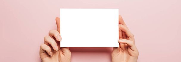 Female hands hold a blank sheet of paper on a pink background. Advertising space - Zdjęcie, obraz