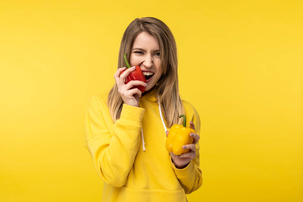 Photo of attractive lady holds papers and bites it with pleasure. Wears casual yellow hoody, isolated yellow color background - Photo, Image