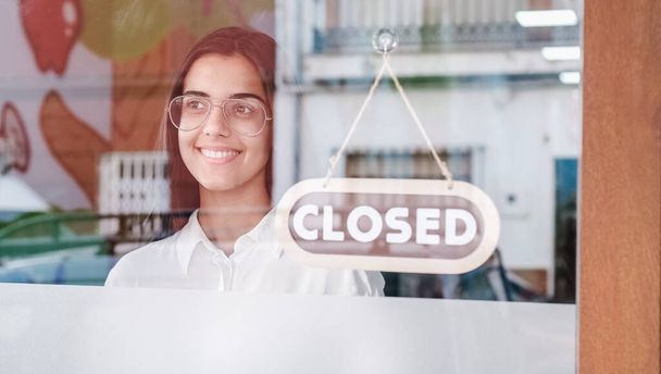 Happy small business girl changing closed to open sign on window smiling looking outside - Photo, Image