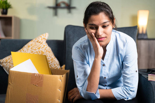 Preoccupata giovane donna d'affari seduta tristemente sul divano a casa a causa della perdita del lavoro, del lavoro o licenziata dal lavoro - Foto, immagini