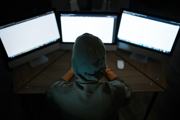 フードの男性のインターネットハッカーモニターに座って、バックビュー。職場での違法Webプログラマー、犯罪者の職業。データハッキングサイバーセキュリティ - 写真・画像