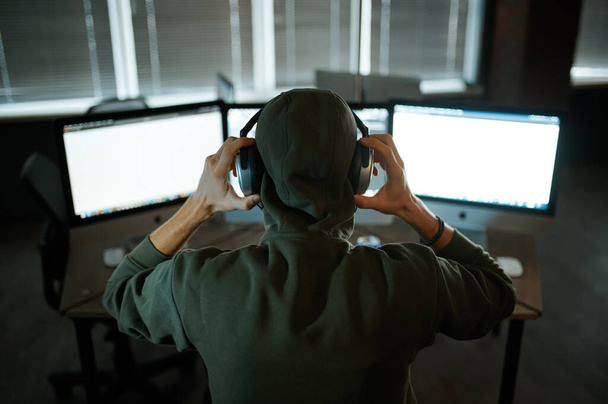 フードとヘッドフォンの男性のインターネットハッカーは、コンピュータ上で動作します。職場での違法Webプログラマー、犯罪者の職業。データハッキングサイバーセキュリティ - 写真・画像