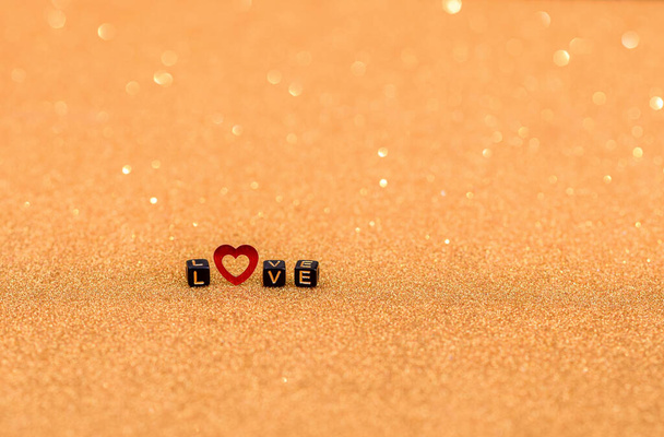 Het woord liefde is neergelegd in houten letters en een rood hart op een gouden achtergrond met lovertjes. Bokeh en selectieve deconcentratie. - Foto, afbeelding