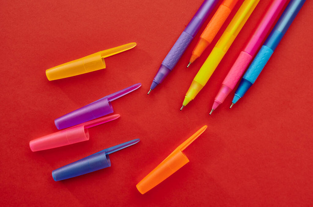 Kleurrijke pennen met caps close-up, rode achtergrond. Kantoorbenodigdheden, school- en onderwijsbenodigdheden, schrijf- en tekengereedschap - Foto, afbeelding