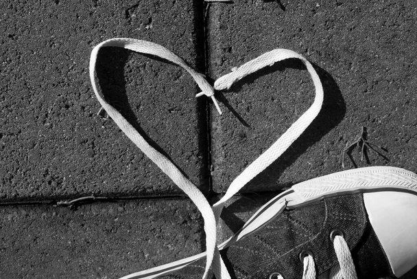 Coeur de lacet près d'une chaussure sur le trottoir, noir et blanc - Photo, image