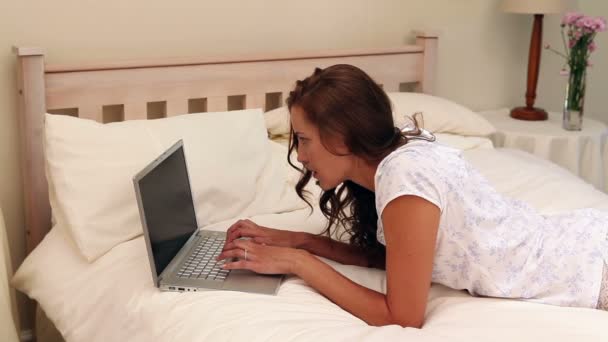 Pretty woman lying on bed using her laptop - Záběry, video