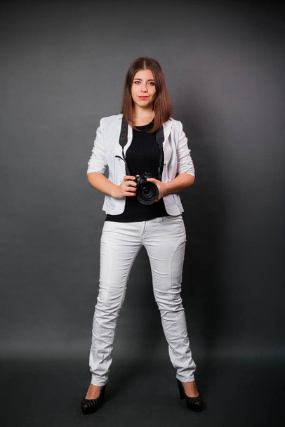 A woman in a white suit with a camera in her hands posing while standing on a black background. Contemporary photographer in the studio. - Fotoğraf, Görsel