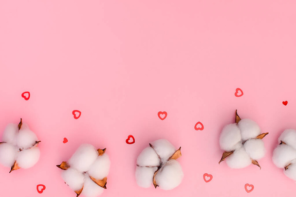 Flores de algodón y corazones pequeños sobre un fondo rosa. Felicidades por el Día de San Valentín. vista superior - Foto, Imagen