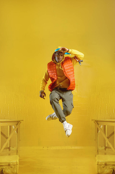 Młody raper skacze w studio w żółtych odcieniach. Hip-hop wykonawca, rap piosenkarz, break-dance wykonywania, rozrywkowy styl życia - Zdjęcie, obraz