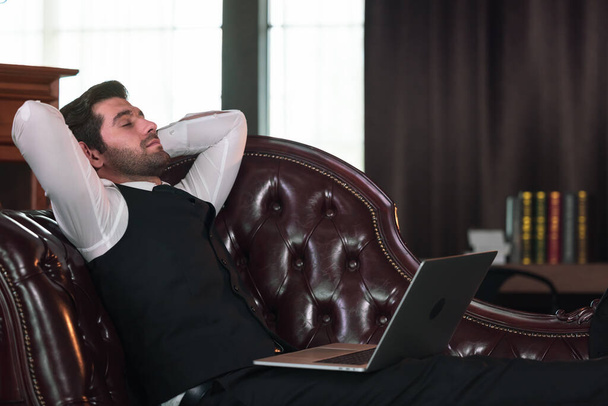 Επιχειρηματίας ξαπλωμένος στον καναπέ και κρατώντας φορητό υπολογιστή. - Φωτογραφία, εικόνα