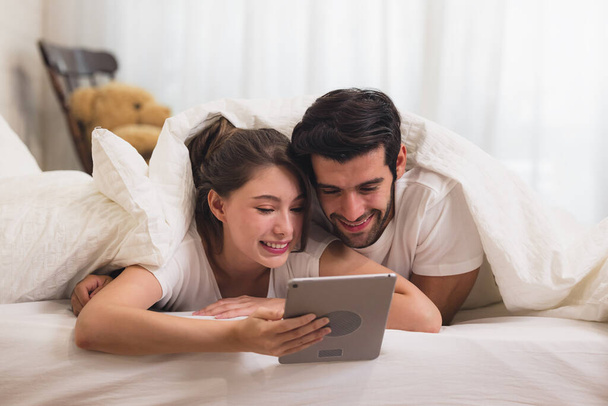 Κοντινό πλάνο Νεαρό γλυκό ζευγάρι στο κρεβάτι βλέποντας κάτι στο Tablet Gadget, χαλαρώνοντας στην κρεβατοκάμαρα. - Φωτογραφία, εικόνα
