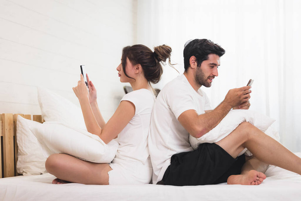 Міленіалістична пара в сварці, лежачи в ліжку назад до спини, використовуючи мобільні телефони
 - Фото, зображення