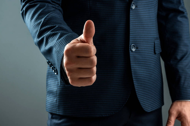 Male hand in suit shows thumbs up gesture on gray background. Concept ok, approval, close-up - Foto, Bild