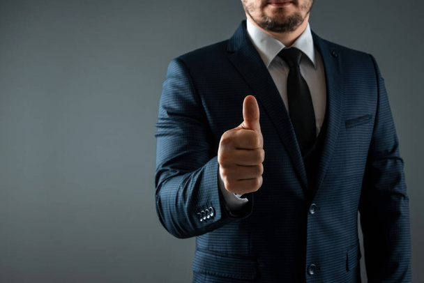 Male hand in suit shows thumbs up gesture on gray background. Concept ok, approval, close-up - Foto, Imagen