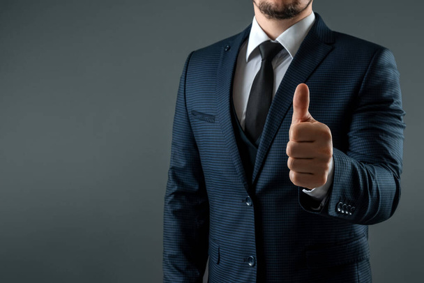 Male hand in suit shows thumbs up gesture on gray background. Concept ok, approval, close-up - Foto, Imagen
