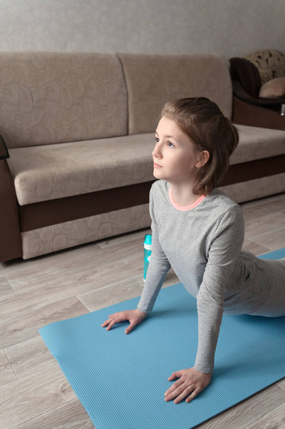 Дівчина-підліток робить фізичні вправи, практикуючи йогу вдома. Здоровий спосіб життя. Тренування вдома. Домашній інтер'єр, природне світло
 - Фото, зображення