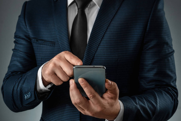 A businessman in a business suit holds a smartphone in his hands. Uses the Internet to work and communicate with partners. Online business concept, remote work, freelance. Close-up - Foto, imagen