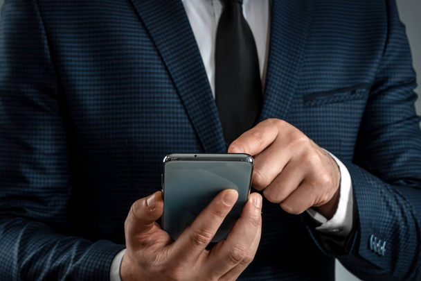 A businessman in a business suit holds a smartphone in his hands. Uses the Internet to work and communicate with partners. Online business concept, remote work, freelance. Close-up - Foto, Imagem