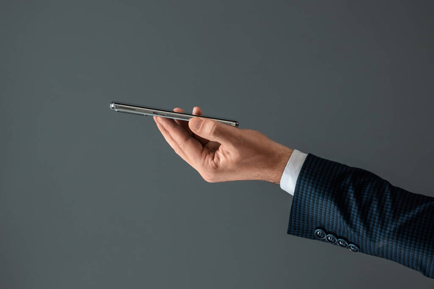 The hand of a businessman in a business suit holds a smartphone horizontally side view. Close-up - Foto, immagini