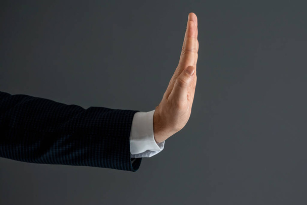 Male hand in a suit shows the palm of the stop gesture on a gray background. Stop concept, close-up - Fotó, kép