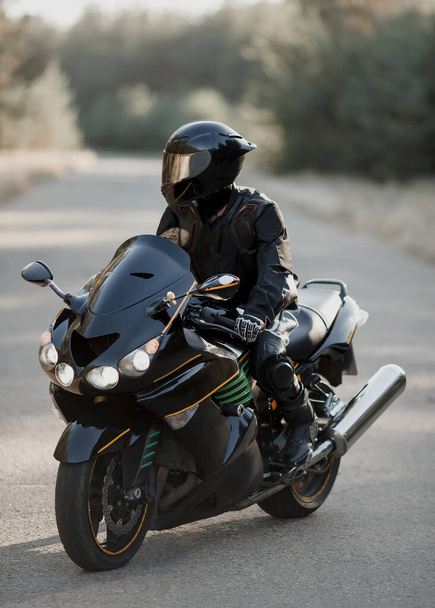 Kasklı siyah motosiklet sürücüsü bulanık arka planlı yolda - Fotoğraf, Görsel
