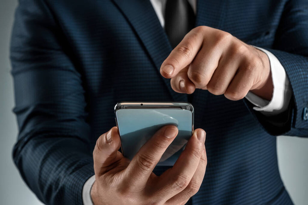 A businessman in a business suit holds a smartphone in his hands. Uses the Internet to work and communicate with partners. Online business concept, remote work, freelance. Close-up - Photo, Image