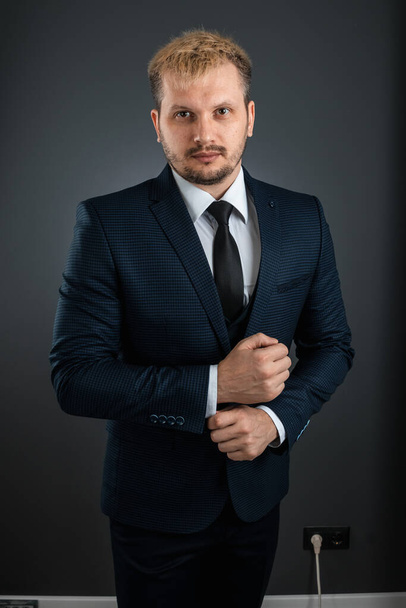 A handsome well-groomed man in a business suit stands on a gray background. Concept businessman, business communication - Fotografie, Obrázek