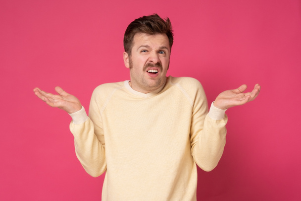 Young confused man shrugging shoulders, spreading hands isolated on pink background - Photo, Image