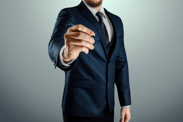 A man in a business suit holds out his hand with a ballpoint pen, writes in the air. Stock for business concept. Close-up, copy space - Valokuva, kuva