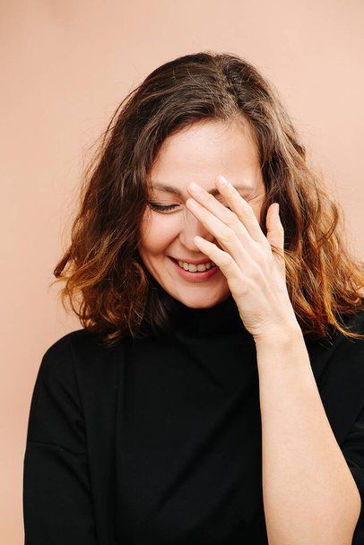 Laughing middle aged woman with her eyes closed, hand covering face. - Foto, imagen