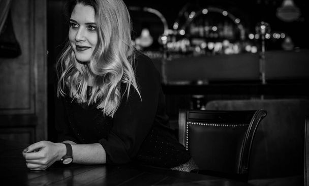 Young elegant plus size woman in cozy atmosphere restaurant. Lady wait on a date in romantic mood. Portrait in deep vintage tones - Photo, Image