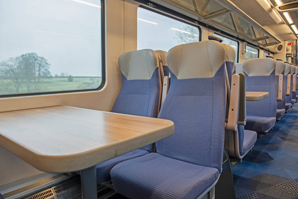 座席とテーブルの行を持つ無人通勤電車の中のインテリアの眺め - 写真・画像
