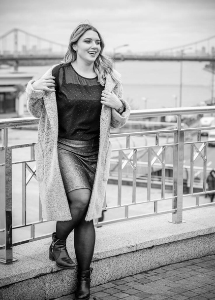 A woman of plus size, American or European appearance walks in the city enjoying life. A young lady with excess weight, stylishly dressed in coat at the center of the city. Natural beauty - Fotó, kép