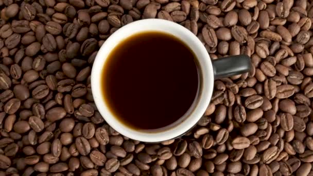 Kopje koffie met vers gebrande koffiebonen achtergrond, close-up cirkelvormige rotatie, hoge hoek uitzicht - Video