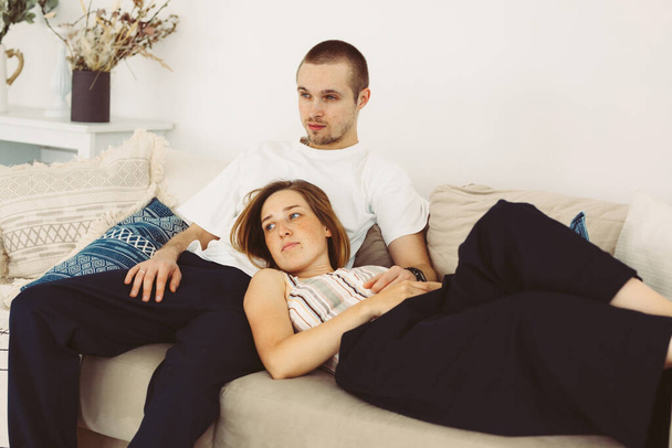 young man sits on sofa, woman lies nearby, leaning against him. living room, interior, rest, family - Fotoğraf, Görsel