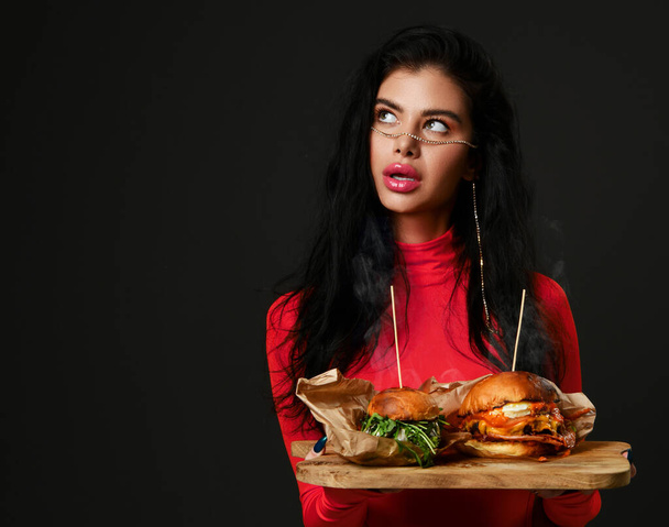 Beautiful woman hold two home made burger sandwiches cheeseburger with hot steam smoke in pink red blouse looking at the corner - Foto, immagini