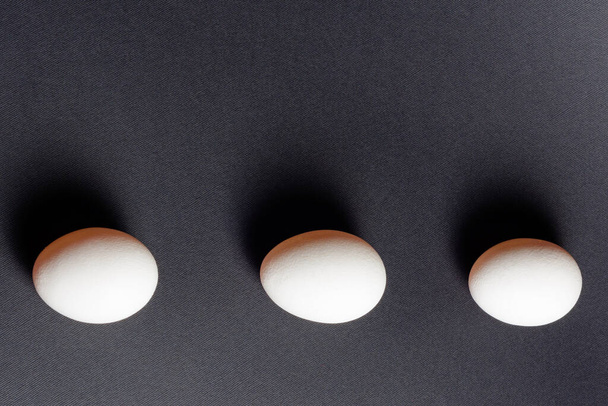 Siyah zemin üzerinde üç beyaz yumurta, 2021 proteini bakımından zengin beslenme ve sağlıklı yiyecekler. - Fotoğraf, Görsel