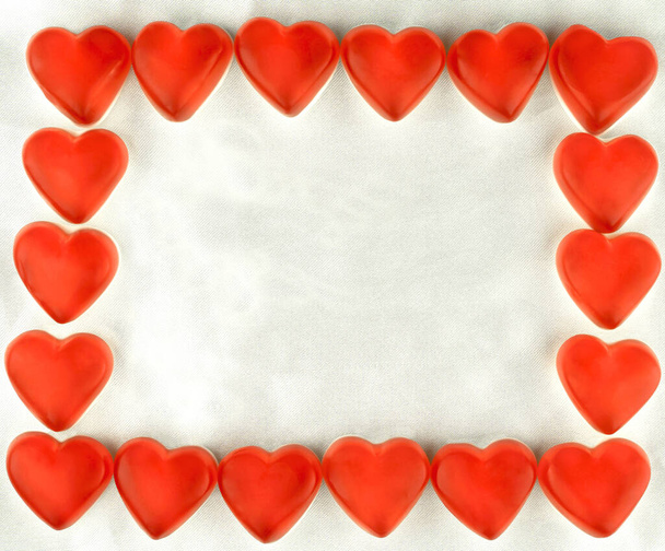 Piros cukorka szív a háttérben a fehér selyem. Üdvözlőlap Valentin nap, évforduló, meghívó. Keret a szöveghez vagy fényképhez - Fotó, kép