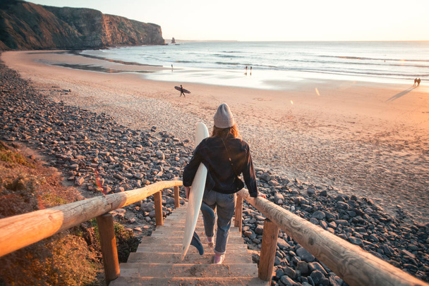 Young woman surfer walk down to beach at sunrise - Фото, зображення