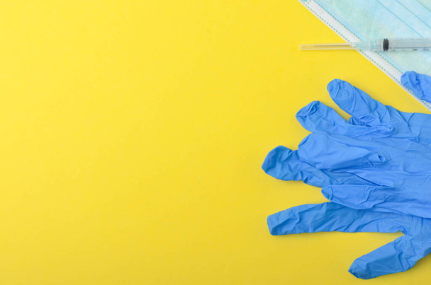Medical glove with syringe and medical face mask on yellow background. Top view and selective focus. - Photo, Image